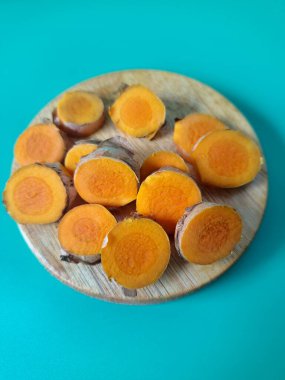 Servis tahtasında taze zerdeçal yumrusu dilimleri. Zerdeçal birçok sağlık yararına sahip bir bitkisel bitkidir. Zerdeçal sıklıkla geleneksel tıpta ve yemek pişirmede bir tat ve doğal renklendirme olarak kullanılır.