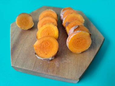 Servis tahtasında taze zerdeçal yumrusu dilimleri. Bu baharat Asya mutfağında yaygın olarak kullanılır, özellikle köri gibi yemeklerde tat ve renk için. Zerdeçal ayrıca aktif bileşik curkiminle birlikte tıbbi özelliklere de sahiptir.