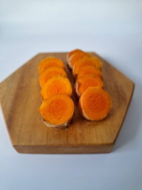 Servis tahtasında taze zerdeçal yumrusu dilimleri. Bu baharat Asya mutfağında yaygın olarak kullanılır, özellikle köri gibi yemeklerde tat ve renk için. Zerdeçal ayrıca aktif bileşik curkiminle birlikte tıbbi özelliklere de sahiptir.