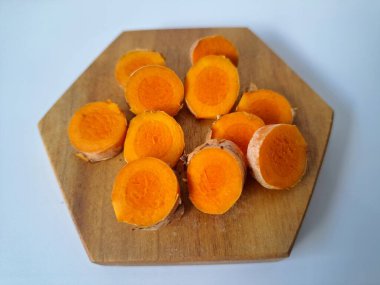 Servis tahtasında taze zerdeçal yumrusu dilimleri. Bu baharat Asya mutfağında yaygın olarak kullanılır, özellikle köri gibi yemeklerde tat ve renk için. Zerdeçal ayrıca aktif bileşik curkiminle birlikte tıbbi özelliklere de sahiptir.