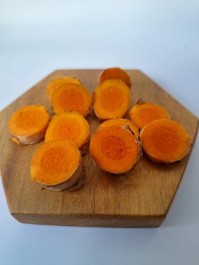 Servis tahtasında taze zerdeçal yumrusu dilimleri. Bu baharat Asya mutfağında yaygın olarak kullanılır, özellikle köri gibi yemeklerde tat ve renk için. Zerdeçal ayrıca aktif bileşik curkiminle birlikte tıbbi özelliklere de sahiptir.