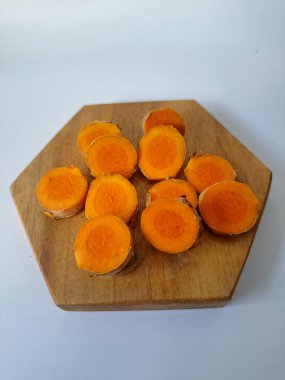 Servis tahtasında taze zerdeçal yumrusu dilimleri. Zerdeçal birçok sağlık yararına sahip bir bitkisel bitkidir. Zerdeçal sıklıkla geleneksel tıpta ve yemek pişirmede bir tat ve doğal renklendirme olarak kullanılır.