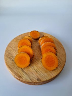 Servis tahtasında taze zerdeçal yumrusu dilimleri. Bu baharat Asya mutfağında yaygın olarak kullanılır, özellikle köri gibi yemeklerde tat ve renk için. Zerdeçal ayrıca aktif bileşik curkiminle birlikte tıbbi özelliklere de sahiptir.