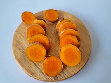 Servis tahtasında taze zerdeçal yumrusu dilimleri. Bu baharat Asya mutfağında yaygın olarak kullanılır, özellikle köri gibi yemeklerde tat ve renk için. Zerdeçal ayrıca aktif bileşik curkiminle birlikte tıbbi özelliklere de sahiptir.