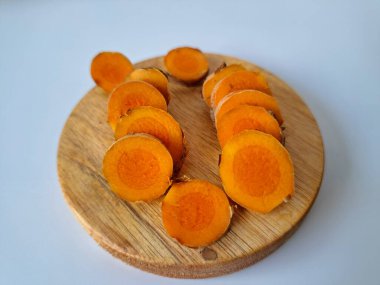 Servis tahtasında taze zerdeçal yumrusu dilimleri. Bu baharat Asya mutfağında yaygın olarak kullanılır, özellikle köri gibi yemeklerde tat ve renk için. Zerdeçal ayrıca aktif bileşik curkiminle birlikte tıbbi özelliklere de sahiptir.