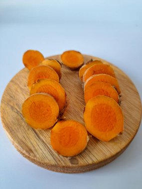 Servis tahtasında taze zerdeçal yumrusu dilimleri. Zerdeçal birçok sağlık yararına sahip bir bitkisel bitkidir. Zerdeçal sıklıkla geleneksel tıpta ve yemek pişirmede bir tat ve doğal renklendirme olarak kullanılır.