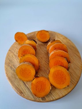 Servis tahtasında taze zerdeçal yumrusu dilimleri. Bu baharat Asya mutfağında yaygın olarak kullanılır, özellikle köri gibi yemeklerde tat ve renk için. Zerdeçal ayrıca aktif bileşik curkiminle birlikte tıbbi özelliklere de sahiptir.