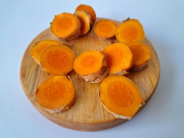 Servis tahtasında taze zerdeçal yumrusu dilimleri. Bu baharat Asya mutfağında yaygın olarak kullanılır, özellikle köri gibi yemeklerde tat ve renk için. Zerdeçal ayrıca aktif bileşik curkiminle birlikte tıbbi özelliklere de sahiptir.