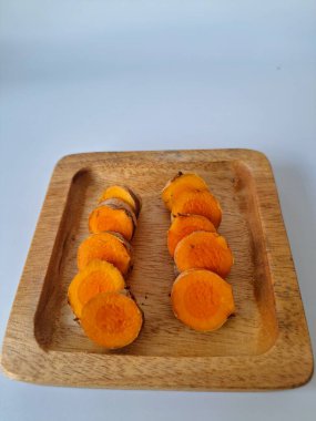 Servis tahtasında taze zerdeçal yumrusu dilimleri. Bu baharat Asya mutfağında yaygın olarak kullanılır, özellikle köri gibi yemeklerde tat ve renk için. Zerdeçal ayrıca aktif bileşik curkiminle birlikte tıbbi özelliklere de sahiptir.