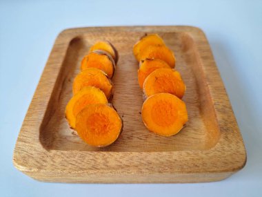 Servis tahtasında taze zerdeçal yumrusu dilimleri. Bu baharat Asya mutfağında yaygın olarak kullanılır, özellikle köri gibi yemeklerde tat ve renk için. Zerdeçal ayrıca aktif bileşik curkiminle birlikte tıbbi özelliklere de sahiptir.