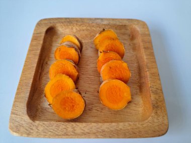 Servis tahtasında taze zerdeçal yumrusu dilimleri. Zerdeçal birçok sağlık yararına sahip bir bitkisel bitkidir. Zerdeçal sıklıkla geleneksel tıpta ve yemek pişirmede bir tat ve doğal renklendirme olarak kullanılır.