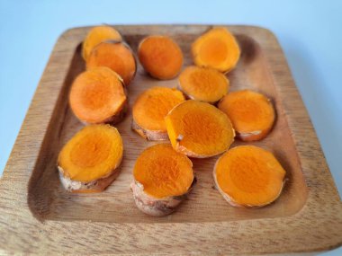 Servis tahtasında taze zerdeçal yumrusu dilimleri. Bu baharat Asya mutfağında yaygın olarak kullanılır, özellikle köri gibi yemeklerde tat ve renk için. Zerdeçal ayrıca aktif bileşik curkiminle birlikte tıbbi özelliklere de sahiptir.