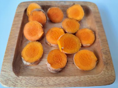 Servis tahtasında taze zerdeçal yumrusu dilimleri. Zerdeçal birçok sağlık yararına sahip bir bitkisel bitkidir. Zerdeçal sıklıkla geleneksel tıpta ve yemek pişirmede bir tat ve doğal renklendirme olarak kullanılır.