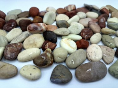Beyaz arka planda izole edilmiş renkli çakıl taşı. Renkli çakıl taşlarının çeşitli dekoratif ve işlevsel kullanımları vardır, özellikle bahçe düzenlemeleri ve bahçecilikte.