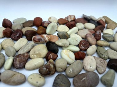 Beyaz arka planda izole edilmiş renkli çakıl taşı. Renkli çakıl taşlarının çeşitli dekoratif ve işlevsel kullanımları vardır, özellikle bahçe düzenlemeleri ve bahçecilikte.