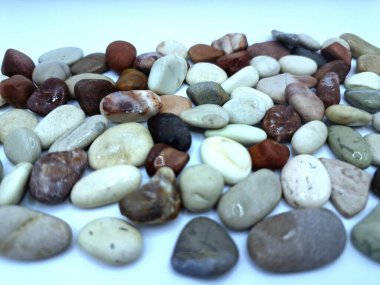Beyaz arka planda izole edilmiş renkli çakıl taşı. Renkli çakıl taşlarının çeşitli dekoratif ve işlevsel kullanımları vardır, özellikle bahçe düzenlemeleri ve bahçecilikte.