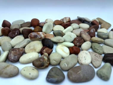 Beyaz arka planda izole edilmiş renkli çakıl taşı. Renkli çakıl taşlarının çeşitli dekoratif ve işlevsel kullanımları vardır, özellikle bahçe düzenlemeleri ve bahçecilikte.