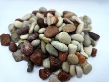 Beyaz arka planda izole edilmiş renkli çakıl taşı. Renkli çakıl taşlarının çeşitli dekoratif ve işlevsel kullanımları vardır, özellikle bahçe düzenlemeleri ve bahçecilikte.