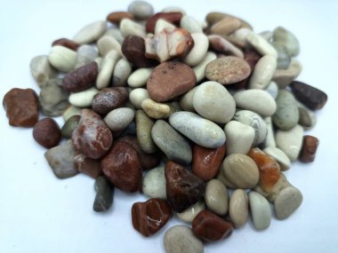 Beyaz arka planda izole edilmiş renkli çakıl taşı. Renkli çakıl taşlarının çeşitli dekoratif ve işlevsel kullanımları vardır, özellikle bahçe düzenlemeleri ve bahçecilikte.