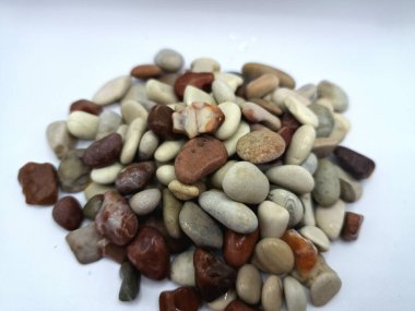 Beyaz arka planda izole edilmiş renkli çakıl taşı. Renkli çakıl taşlarının çeşitli dekoratif ve işlevsel kullanımları vardır, özellikle bahçe düzenlemeleri ve bahçecilikte.