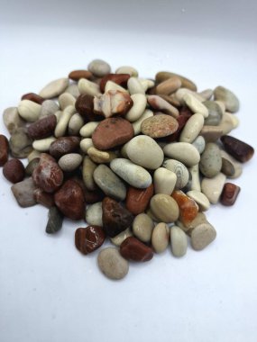 Beyaz arka planda izole edilmiş renkli çakıl taşı. Renkli çakıl taşlarının çeşitli dekoratif ve işlevsel kullanımları vardır, özellikle bahçe düzenlemeleri ve bahçecilikte.