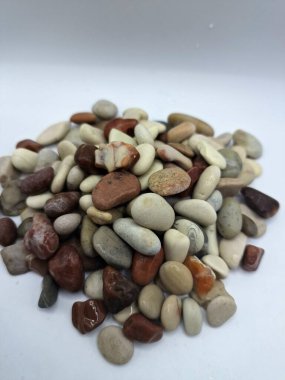 Beyaz arka planda izole edilmiş renkli çakıl taşı. Renkli çakıl taşlarının çeşitli dekoratif ve işlevsel kullanımları vardır, özellikle bahçe düzenlemeleri ve bahçecilikte.