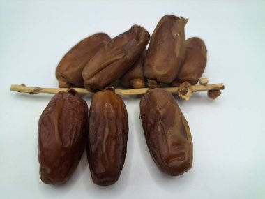 Beyaz arka planda tarihler. Hurma ağacının meyveleri, yumuşak ve tatlı bir ağaçtır. Genellikle ağaçtaki kümelerde bulunurlar ve kahverengiye döndüklerinde ve buruşuklaştıklarında büyük buruşmuş kuru üzümlere benzerler.