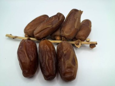 Beyaz arka planda tarihler. Hurma ağacının meyveleri, yumuşak ve tatlı bir ağaçtır. Genellikle ağaçtaki kümelerde bulunurlar ve kahverengiye döndüklerinde ve buruşuklaştıklarında büyük buruşmuş kuru üzümlere benzerler.