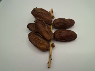 Beyaz arka planda tarihler. Hurma ağacının meyveleri, yumuşak ve tatlı bir ağaçtır. Genellikle ağaçtaki kümelerde bulunurlar ve kahverengiye döndüklerinde ve buruşuklaştıklarında büyük buruşmuş kuru üzümlere benzerler.