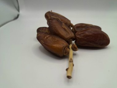 Beyaz arka planda tarihler. Hurma ağacının meyveleri, yumuşak ve tatlı bir ağaçtır. Genellikle ağaçtaki kümelerde bulunurlar ve kahverengiye döndüklerinde ve buruşuklaştıklarında büyük buruşmuş kuru üzümlere benzerler.