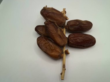 Beyaz arka planda tarihler. Hurma ağacının meyveleri, yumuşak ve tatlı bir ağaçtır. Genellikle ağaçtaki kümelerde bulunurlar ve kahverengiye döndüklerinde ve buruşuklaştıklarında büyük buruşmuş kuru üzümlere benzerler.