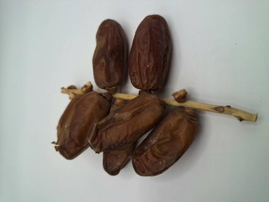 Beyaz arka planda tarihler. Hurma ağacının meyveleri, yumuşak ve tatlı bir ağaçtır. Genellikle ağaçtaki kümelerde bulunurlar ve kahverengiye döndüklerinde ve buruşuklaştıklarında büyük buruşmuş kuru üzümlere benzerler.
