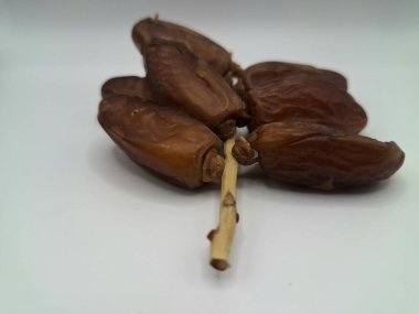 Beyaz arka planda tarihler. Hurma ağacının meyveleri, yumuşak ve tatlı bir ağaçtır. Genellikle ağaçtaki kümelerde bulunurlar ve kahverengiye döndüklerinde ve buruşuklaştıklarında büyük buruşmuş kuru üzümlere benzerler.