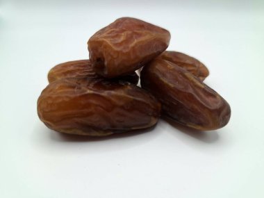 Beyaz arka planda tarihler. Hurma ağacının meyveleri, yumuşak ve tatlı bir ağaçtır. Genellikle ağaçtaki kümelerde bulunurlar ve kahverengiye döndüklerinde ve buruşuklaştıklarında büyük buruşmuş kuru üzümlere benzerler.