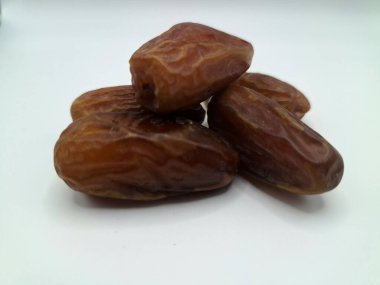 Beyaz arka planda tarihler. Hurma ağacının meyveleri, yumuşak ve tatlı bir ağaçtır. Genellikle ağaçtaki kümelerde bulunurlar ve kahverengiye döndüklerinde ve buruşuklaştıklarında büyük buruşmuş kuru üzümlere benzerler.