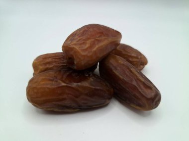 Beyaz arka planda tarihler. Hurma ağacının meyveleri, yumuşak ve tatlı bir ağaçtır. Genellikle ağaçtaki kümelerde bulunurlar ve kahverengiye döndüklerinde ve buruşuklaştıklarında büyük buruşmuş kuru üzümlere benzerler.