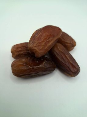 Beyaz arka planda tarihler. Hurma ağacının meyveleri, yumuşak ve tatlı bir ağaçtır. Genellikle ağaçtaki kümelerde bulunurlar ve kahverengiye döndüklerinde ve buruşuklaştıklarında büyük buruşmuş kuru üzümlere benzerler.