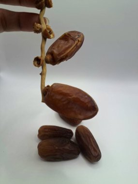 Beyaz arka planda tarihler. Hurma ağacının meyveleri, yumuşak ve tatlı bir ağaçtır. Genellikle ağaçtaki kümelerde bulunurlar ve kahverengiye döndüklerinde ve buruşuklaştıklarında büyük buruşmuş kuru üzümlere benzerler.