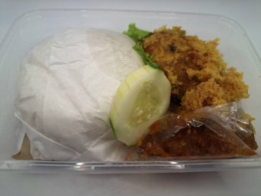 Dilimlenmiş salatalık ve biber sosuyla servis edilen kızarmış tavuk ve pilav plastik bir kabın içinde.