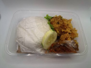 Dilimlenmiş salatalık ve biber sosuyla servis edilen kızarmış tavuk ve pilav plastik bir kabın içinde.