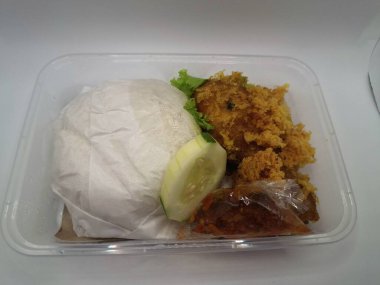 Dilimlenmiş salatalık ve biber sosuyla servis edilen kızarmış tavuk ve pilav plastik bir kabın içinde.