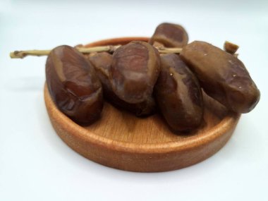Küçük ahşap bir tabakta meyve. Hurma ağacından sarkan tatlı meyveler. Tek bir tohumla çevrili, tatlı, etli, kahverengi, koyu kahverengi ya da sarı renkli bir meyvedir.
