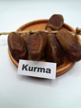 Küçük ahşap bir tabakta meyve. Hurma ağacından sarkan tatlı meyveler. Tek bir tohumla çevrili, tatlı, etli, kahverengi, koyu kahverengi ya da sarı renkli bir meyvedir.