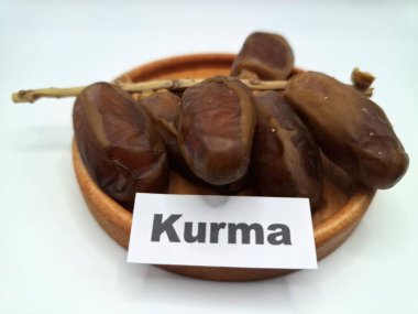 Küçük ahşap bir tabakta meyve. Hurma ağacından sarkan tatlı meyveler. Tek bir tohumla çevrili, tatlı, etli, kahverengi, koyu kahverengi ya da sarı renkli bir meyvedir.