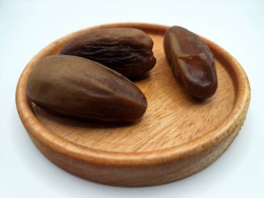Küçük ahşap bir tabakta meyve. Hurma ağacından sarkan tatlı meyveler. Tek bir tohumla çevrili, tatlı, etli, kahverengi, koyu kahverengi ya da sarı renkli bir meyvedir.