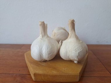 Tahta servis tahtasındaki sarımsak soğanları. Sarımsak, Allium ailesinden gelen soğanlı bir bitkidir. Güçlü, keskin kokusu ve tadı ile karakterize edilir. Sarımsak yaygın olarak mutfak aroması olarak kullanılır ve aynı zamanda tıbbi özelliklere sahiptir.