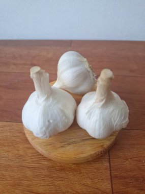 Yuvarlak tahta üzerinde sarımsak. Sarımsak hem aşçılık hem de doğal bir çare olarak çok yönlü bir bileşendir. Yemek pişirmede, sayısız yemeğin ana maddesidir. Soslara, çorbaya ve etlere keskin bir tat katar.