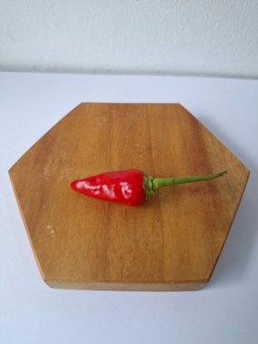 Ahşap servis tahtasında kırmızı kırmızıbiber. Kırmızı biber, acı bir tadı olan ve genellikle yemek ve tıpta kullanılan bir kırmızı biber türüdür. Bu biber ince şekli, parlak kırmızı rengi ve yüksek baharat seviyesi ile bilinir.