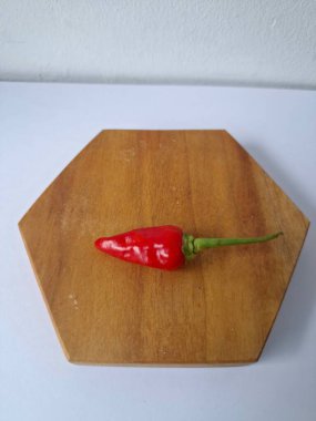 Ahşap servis tahtasında kırmızı kırmızıbiber. Kırmızı biber, acı bir tadı olan ve genellikle yemek ve tıpta kullanılan bir kırmızı biber türüdür. Bu biber ince şekli, parlak kırmızı rengi ve yüksek baharat seviyesi ile bilinir.