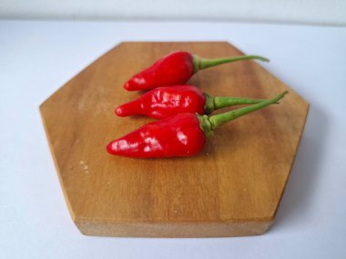 Ahşap servis tahtasında kırmızı kırmızıbiber. Kırmızı biber, acı bir tadı olan ve genellikle yemek ve tıpta kullanılan bir kırmızı biber türüdür. Bu biber ince şekli, parlak kırmızı rengi ve yüksek baharat seviyesi ile bilinir.